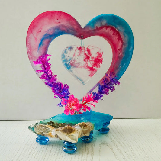A breathtaking two-tone pink and blue resin heart sculpture on a landscape stand